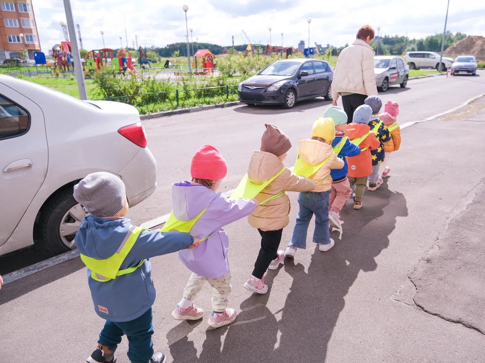 Accompagnateur marche avec une file d'enfants en gilet fluo dans une rue