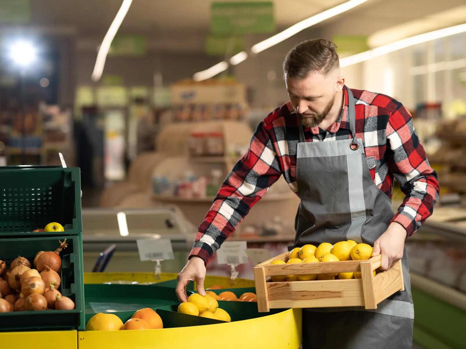 Jeune employé remplit le bac de pommes au rayon fruits et légumes