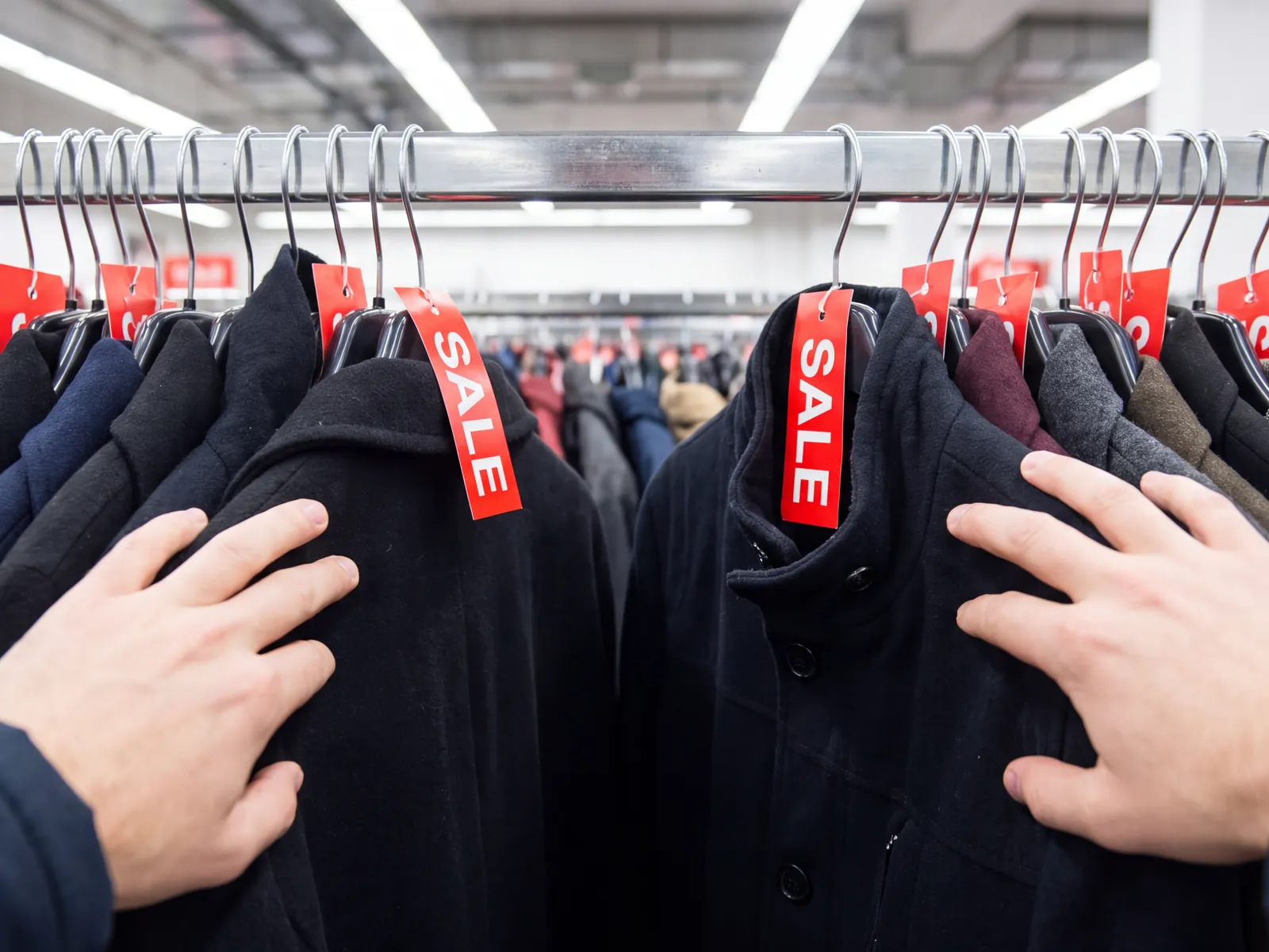 Verkoopster hangt kledingstukken met rode kortingskaartjes terug aan een rek