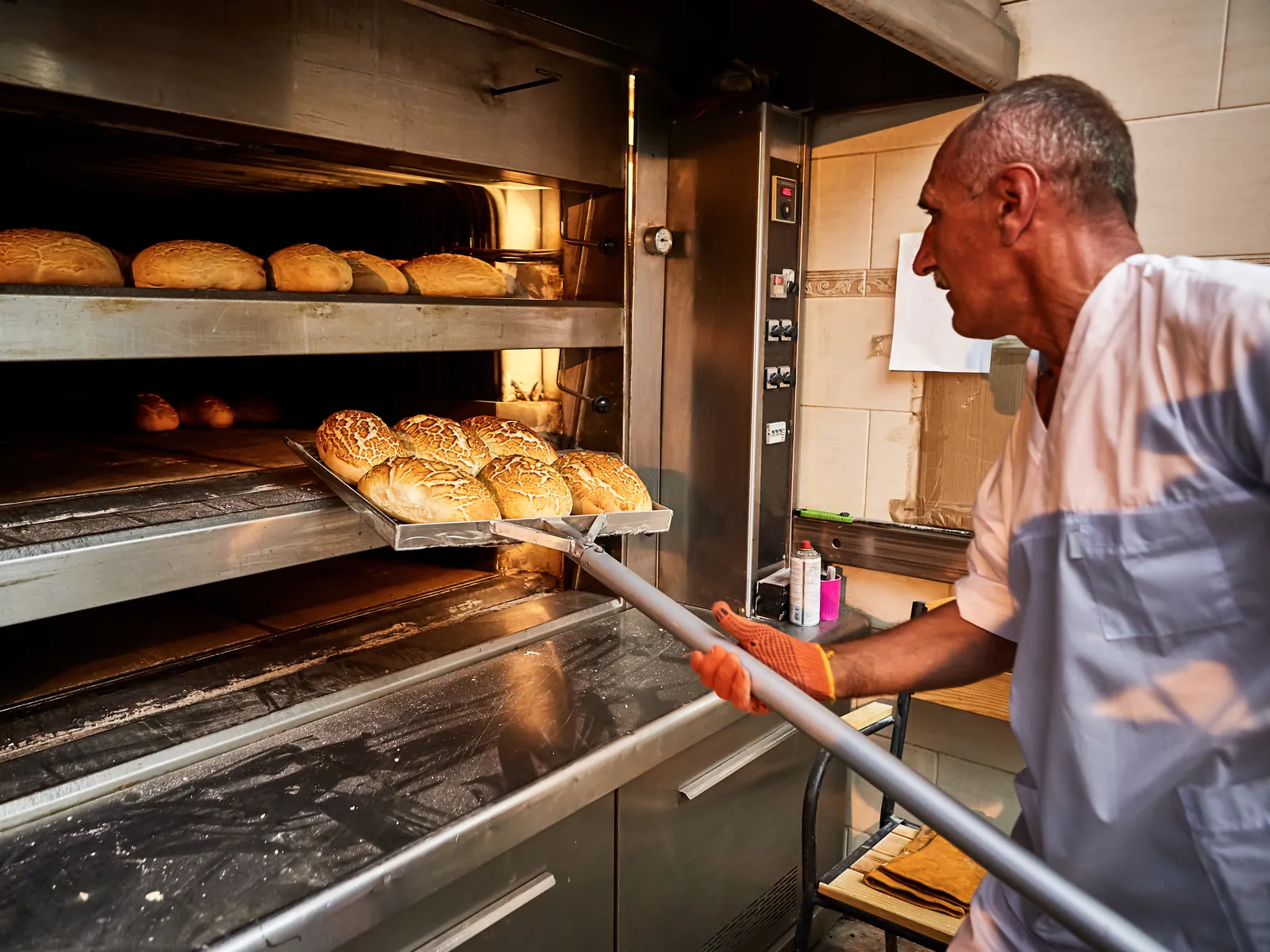 Employée glisse une plaque de pain précuit dans le four de la boulangerie